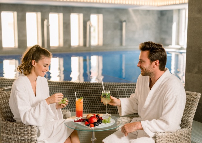 Couple in bathrobes enjoying cocktails by the indoor wellness pool at Bonvital.