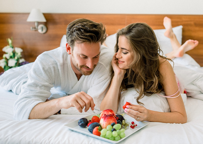Couple relaxing with a fruit platter in a comfortable hotel room at Bonvital Wellness & Gastro Hotel Hévíz as part of the Autumn Wellness Package.